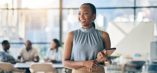 A woman standing and smiling in a busy office building.